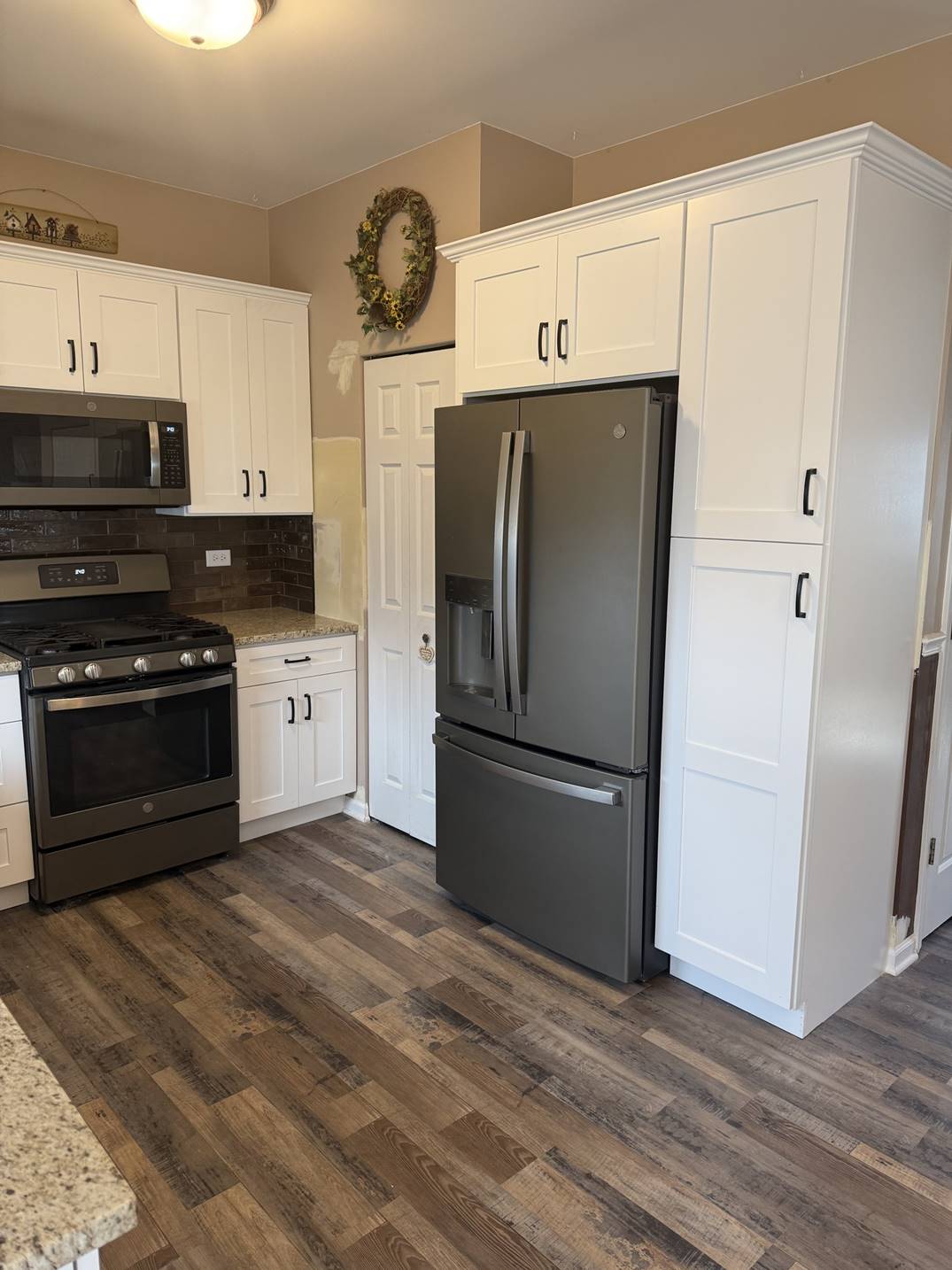 White kitchen cabinetry with a black refrigerator and wood-look floor